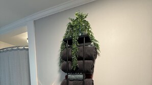 Une étagère fixée au mur, avec des serviettes pliées et une plante en pot.