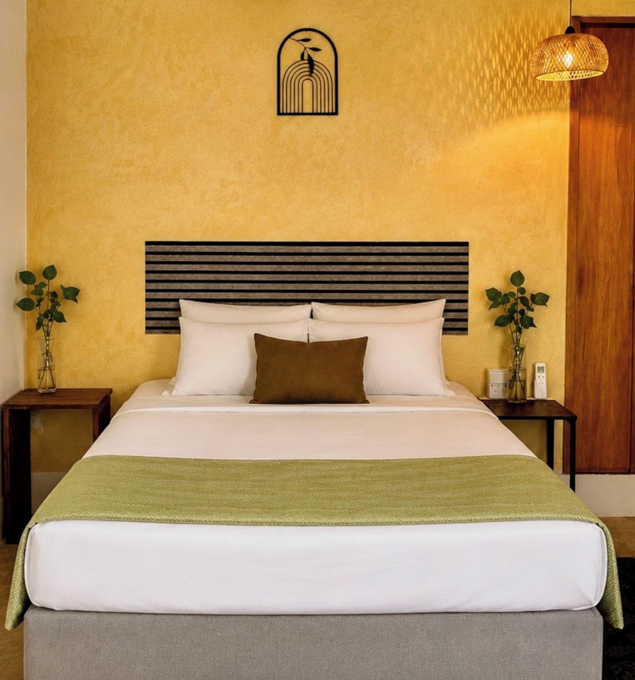 Una cama con cabecera, una mesita de noche con lámpara y un aplique de pared.