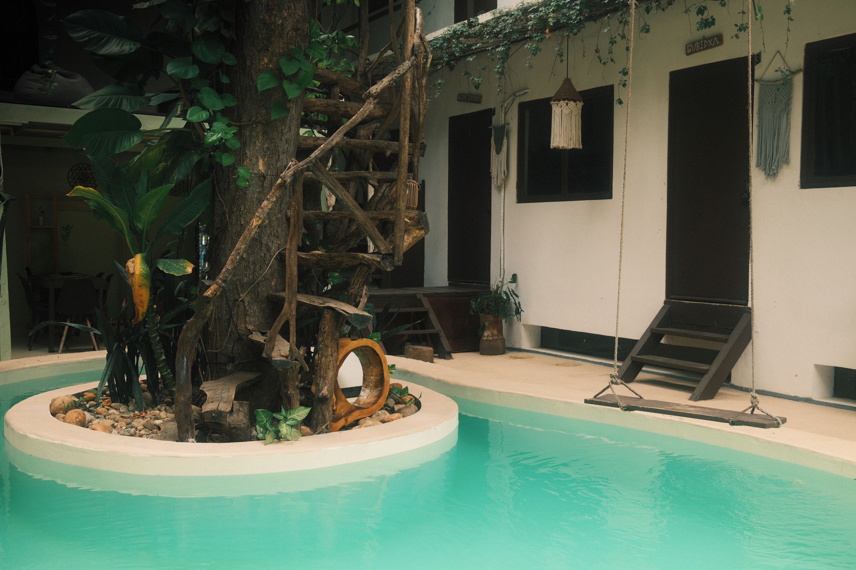 Una piscina interior con una estructura de árbol de madera, sillas de descanso y un columpio colgante.