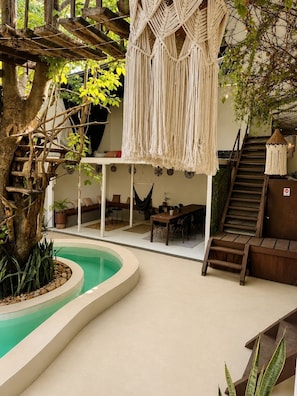 A pool area with macrame hanging decorations, a staircase, and a seating area with a table and chairs. - Casa Alkaia (Puerto Escondido)