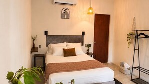 A bedroom with a bed, bedside tables, a ceiling fan, an air conditioning unit, a hanging light fixture, a door, a plant, and a small table. - Casa Ceiba  (Puerto Escondido)