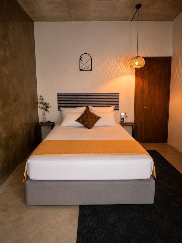 A neatly made bed with a headboard, a bedside table with a lamp, and a wall-mounted clock.