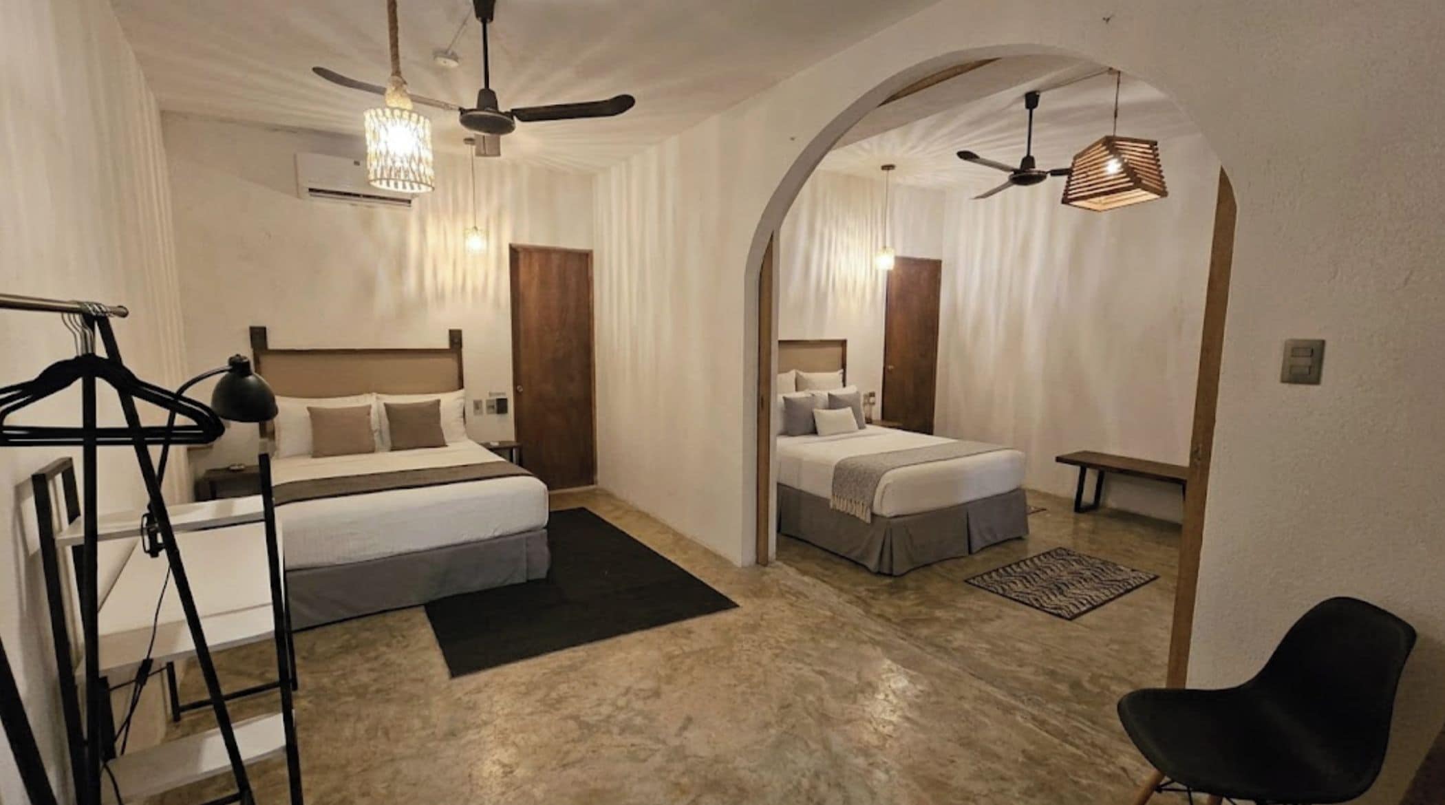 Una habitación de hotel con dos camas, un ventilador de techo, una lámpara colgante y un banco.