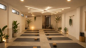 Un estudio de yoga con colchonetas dispuestas en filas, plantas en macetas y una lámpara en el techo.