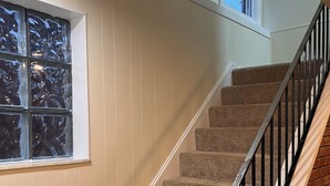 Eine Teppichstiege mit schwarzem Geländer, weißen Wänden und einem Fenster mit Blick auf Bäume.