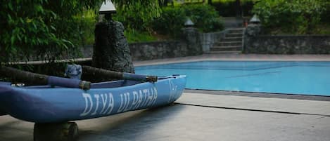 A blue kayak with 'DIVI UL PATHA' written on it, a stone pillar, and a pool in the background.