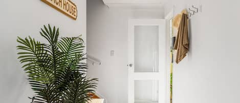 A hallway with a white door, a plant, a wooden sign reading 'BEACH HOUSE', and a towel rack.