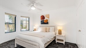 A bedroom with a bed, two bedside tables, a ceiling fan, and two windows with a view. - The Sails 1/21 Beech Street  Evans Head (Evans Head)