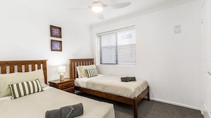 A bedroom with two beds, a ceiling fan, a window with blinds, and a wall-mounted light. - The Sails 1/21 Beech Street  Evans Head (Evans Head)