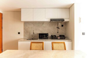 A modern kitchen with white cabinets, a microwave, a gas stove, and two wicker chairs. - Salt Lofts Pererenan (Bali)