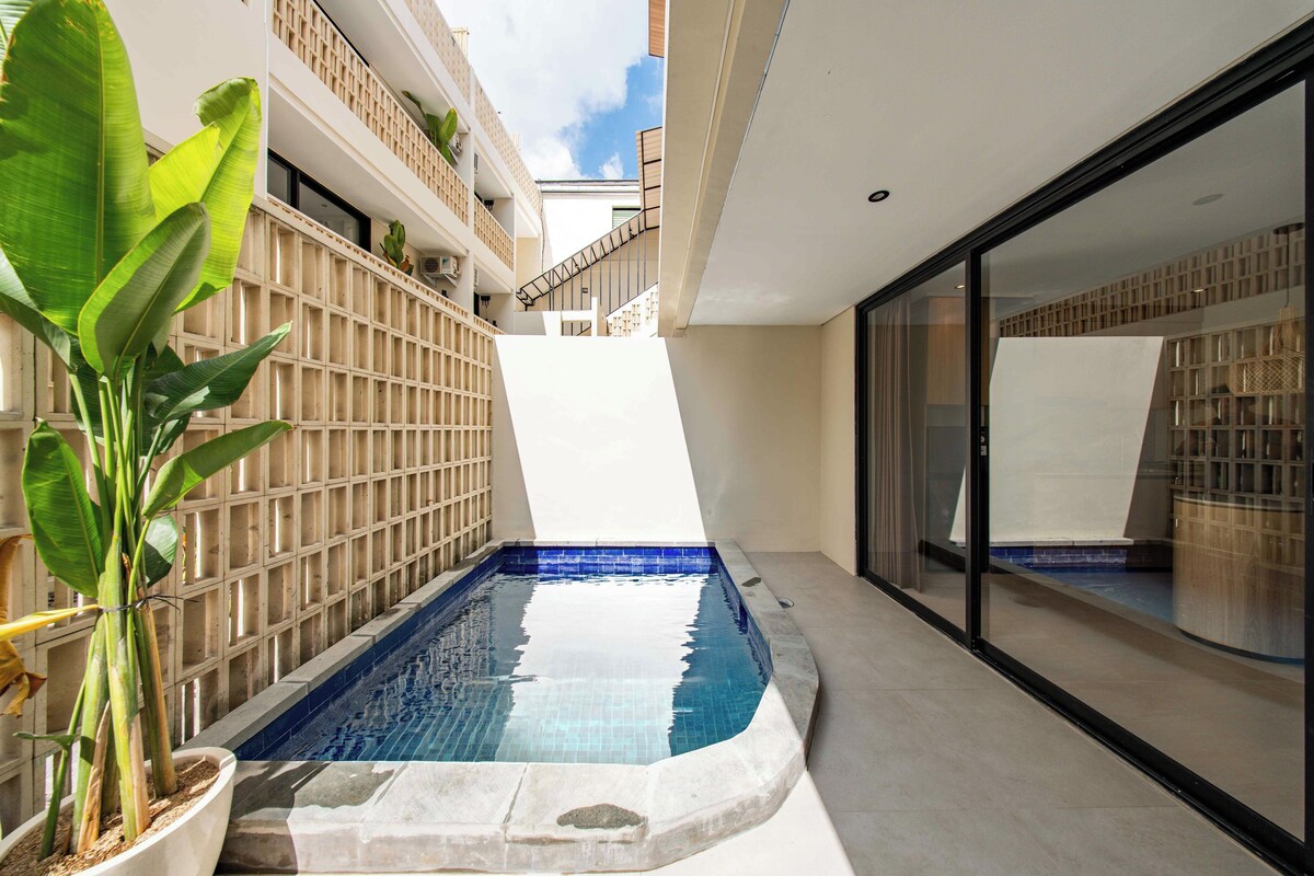 A modern outdoor pool area with a geometric pool design, surrounded by a wooden fence and potted plants.