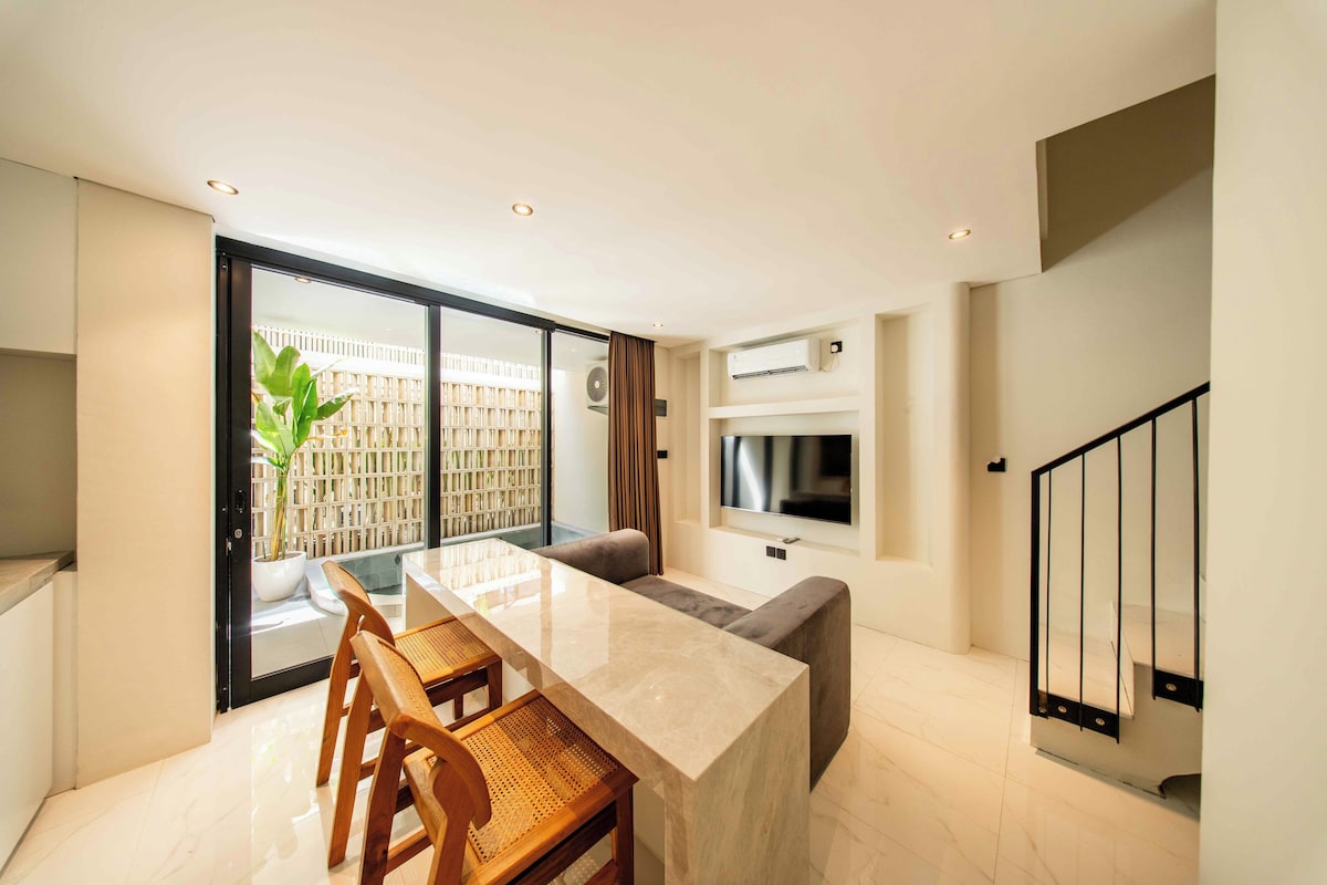 A modern kitchen with a dining area, a large window, and a staircase.