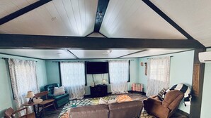 Ein gemütliches Wohnzimmer mit einer Couch, Sesseln, einem Couchtisch und gemusterten Vorhängen.