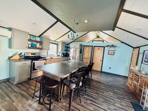 A kitchen with a large island, bar stools, wooden flooring, and a sloped ceiling.