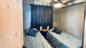 Ein Zimmer mit zwei Betten, einem Deckenventilator, einem Holzschrank und einem Vorhang.