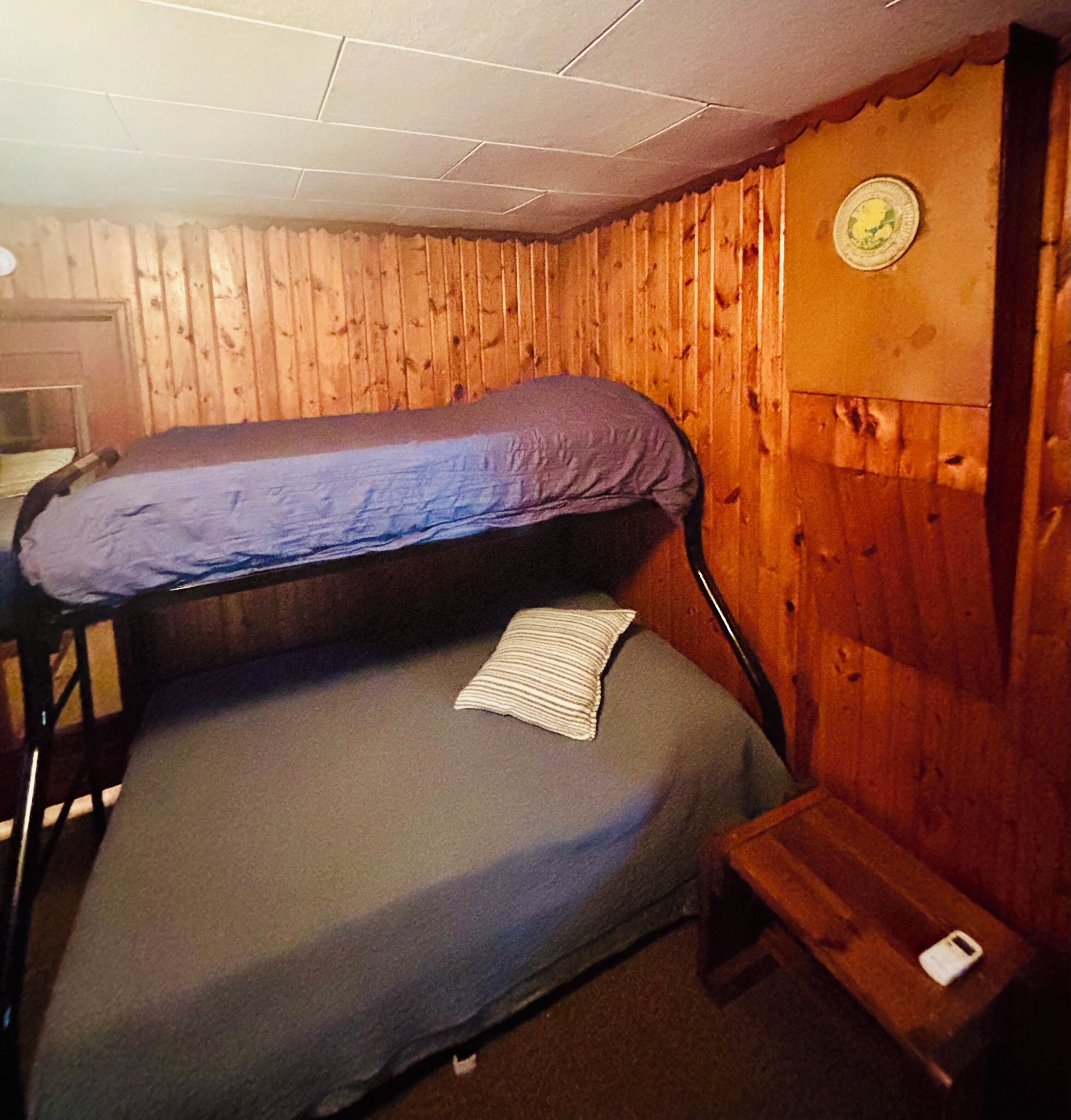 A bunk bed with a pillow and a blanket, wooden walls, a small table, and a wall clock.