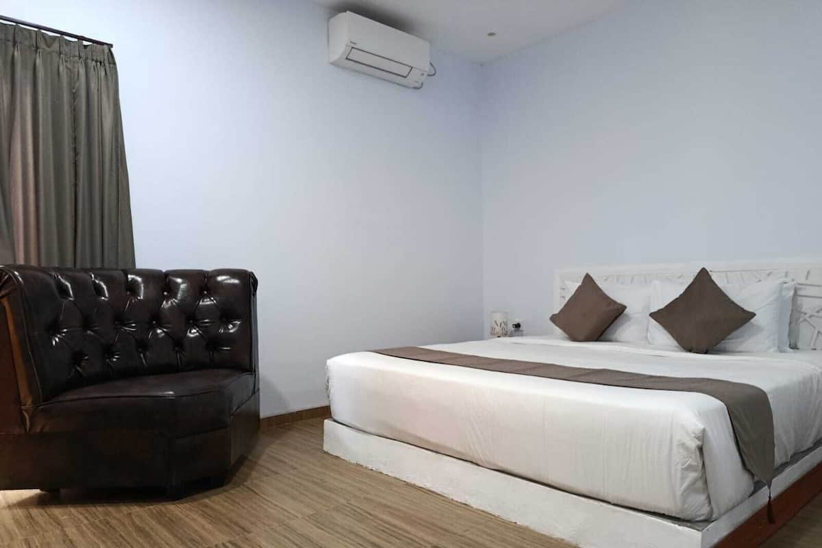 Un dormitorio con cama, un sillón de cuero, cabecera blanca y aire acondicionado en el techo.