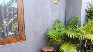 A corner with a window, a small stool, and large green plants. - Sri Asta Guna (Legian)