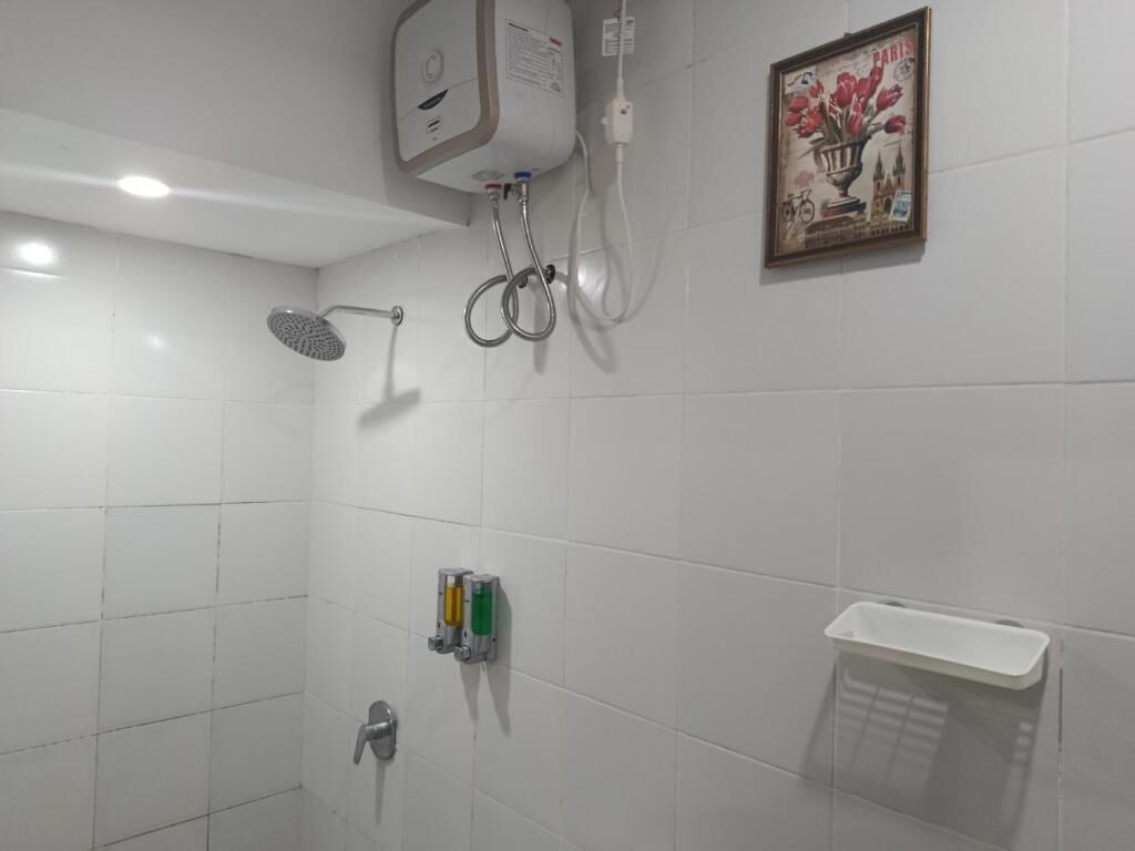Ein Badezimmer mit weißen Fliesen, einer Duschbrause, einem Handtuchhalter, einem Seifenspender und einem gerahmten Bild an der Wand.