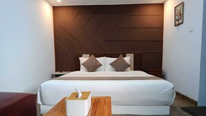 A hotel room with a large bed, a wooden nightstand, a bedside table with a tissue box, and a red couch. - Sri Asta Guna (Legian)