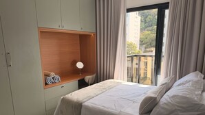 Un dormitorio con cama, un armario de madera, un espejo y una ventana con cortinas.