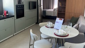 Una cocina moderna con electrodomésticos, un comedor con una mesa lista para dos personas y una sala de estar con un sofá y una estantería.
