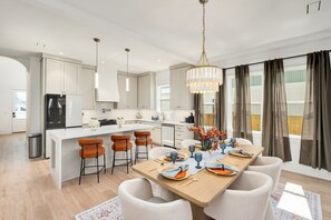 Een moderne keuken met een centraal eiland, barstoelen en een eettafel gedekt voor zes personen.
