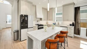 Een moderne keuken met witte kasten, een marmeren eiland en oranje barkrukken.
