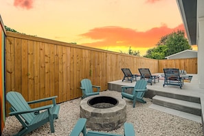 Ein Garten mit Holzzaun, Gartenmöbel, Adirondack-Stühle, einer Feuerstelle und einer Terrasse.