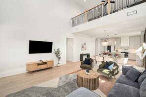 Un salon spacieux doté d’un téléviseur à écran plat, d’une console en bois et d’un coin repas agrémenté d’un lustre.
