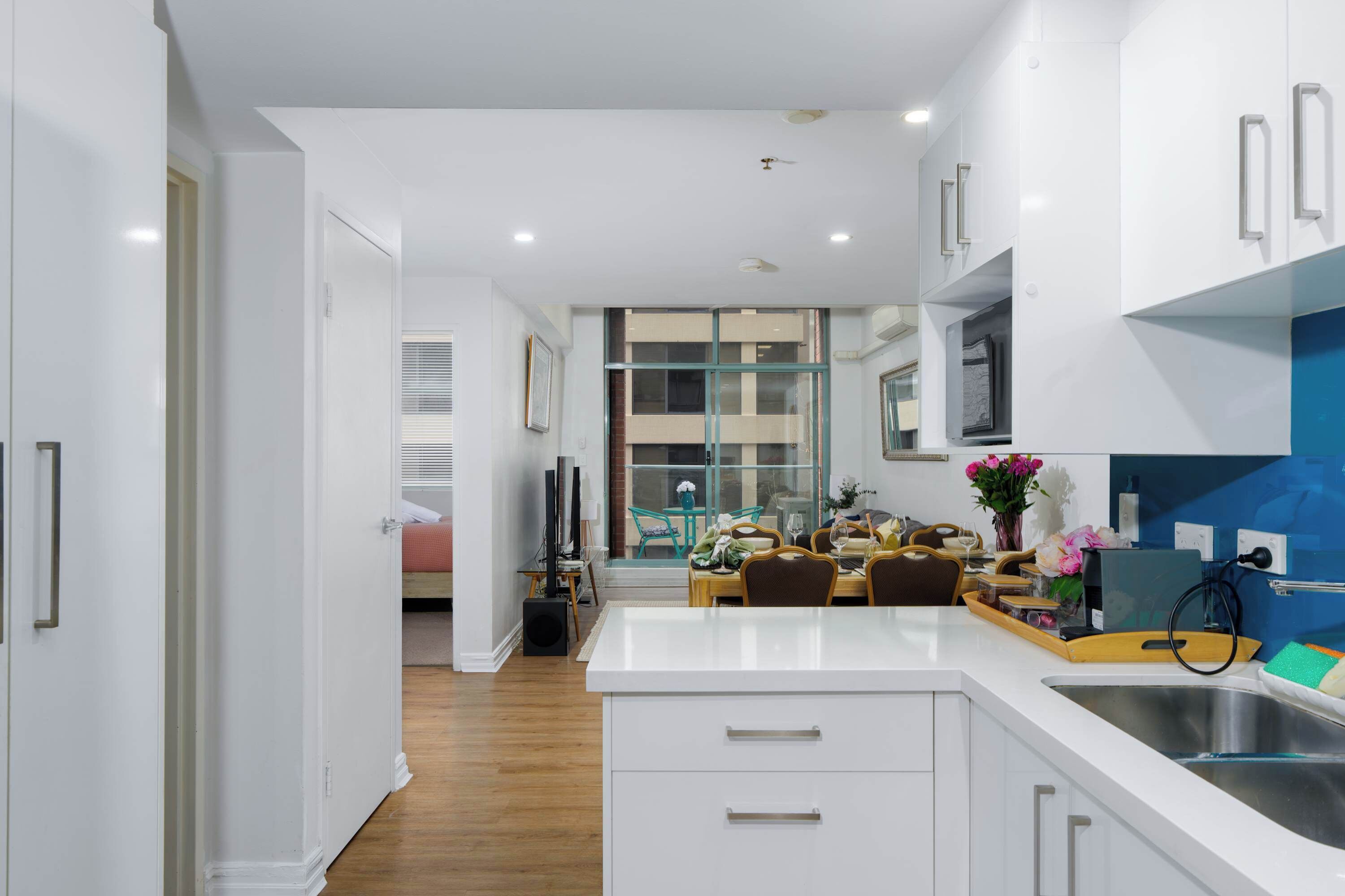 A modern kitchen with white cabinetry, a central island, and a dining area with chairs and a table.