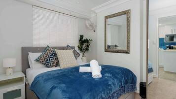 A hotel room with a bed, a bedside table with a lamp, a wall-mounted mirror, and a potted plant.