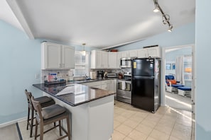 A modern kitchen with white cabinets, a central island with bar stools, a black refrigerator, and a microwave. - Ocean City NJ Beach Block 5BR/2.5BA - Steps to Beach (Ocean City)