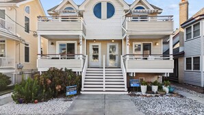 A two-story house with a central entrance, a balcony on each floor, and a small front yard with potted plants. - Ocean City NJ Beach Block 5BR/2.5BA - Steps to Beach (Ocean City)