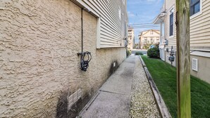 A narrow pathway between two houses with a visible water spigot and a hose on the left. - Ocean City NJ Beach Block 5BR/2.5BA - Steps to Beach (Ocean City)