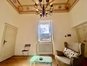 A room with a large window, a radiator, a chandelier, a sofa, and a small table. - Sui Tetti di Marciana Marina (Marciana Marina)