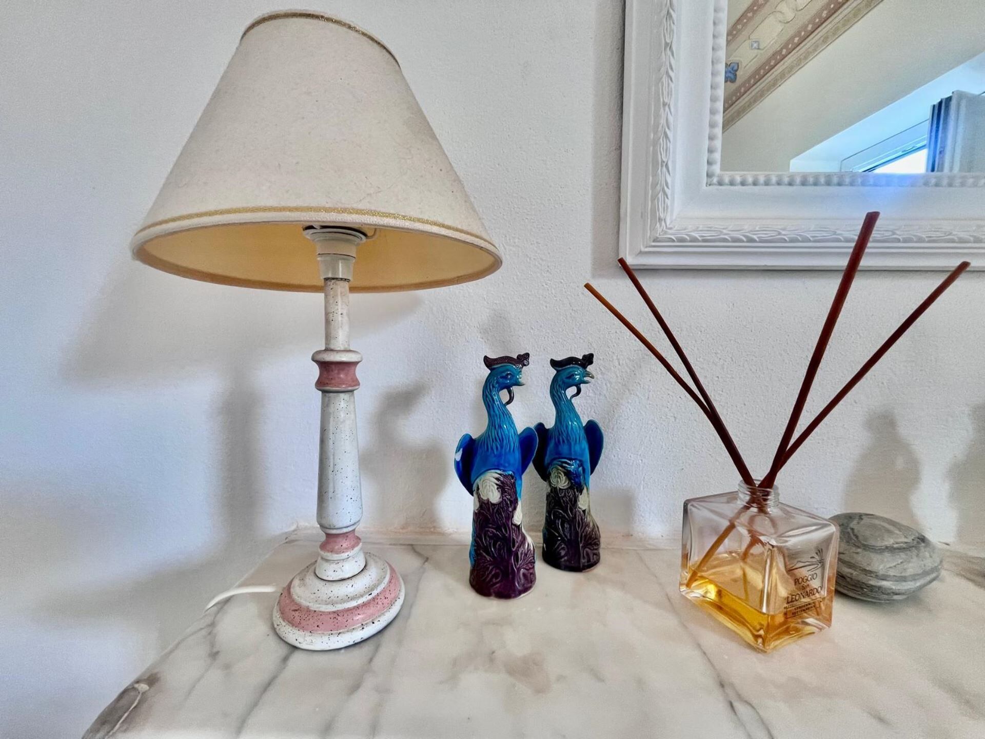 Een lamp, twee decoratieve beeldjes en een parfumflesje op een marmeren oppervlak.