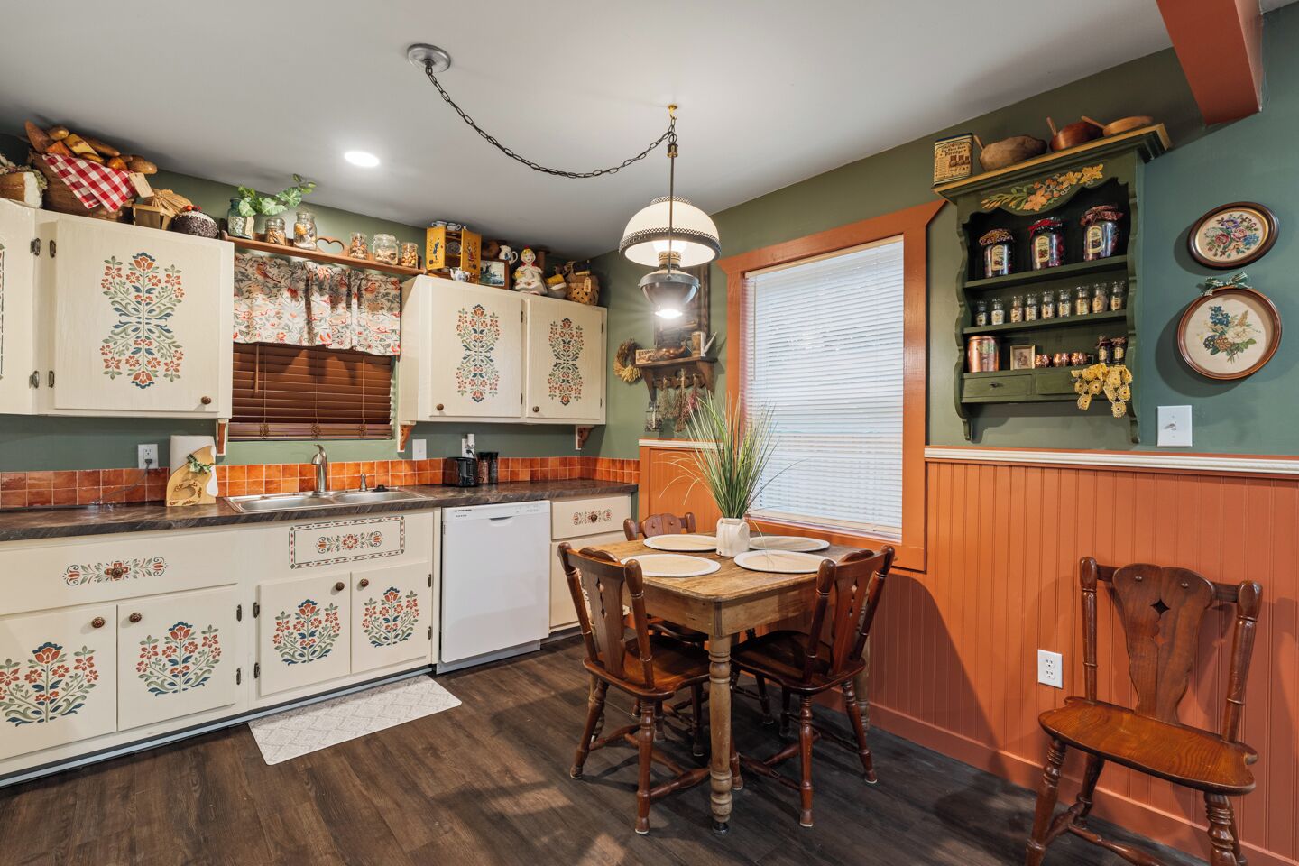 Une cuisine avec des meubles de rangement en bois, une table à manger et une fenêtre avec des stores.