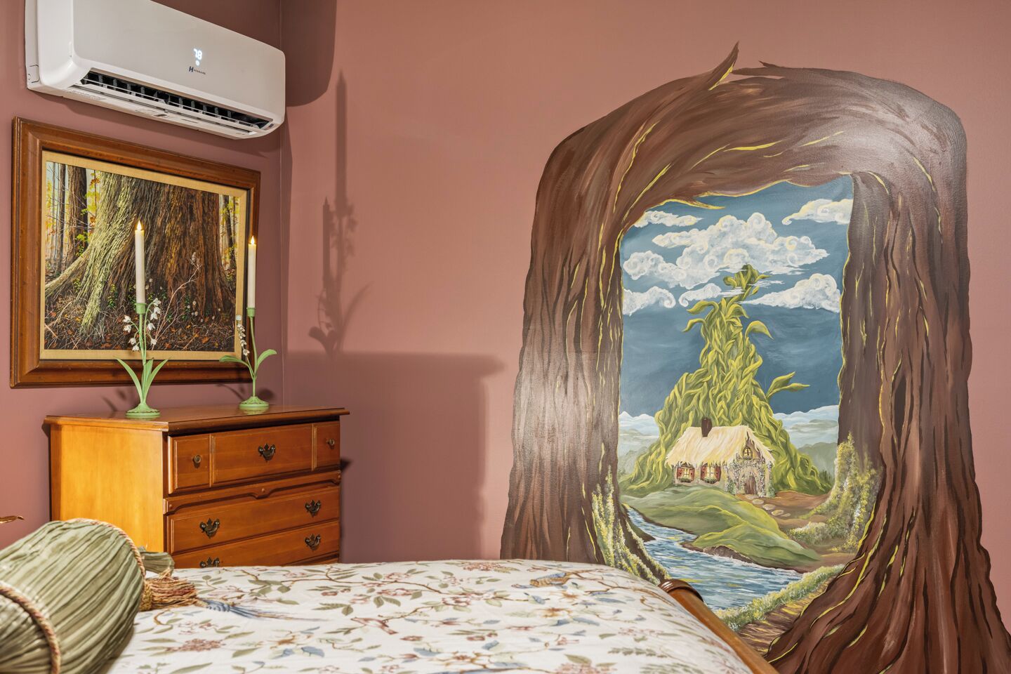 A bedroom with a bed, dresser, and a painting of a forest scene.