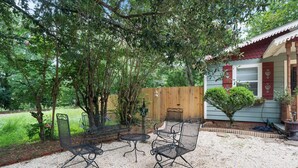 An outdoor seating area with metal chairs and a table, surrounded by trees and a wooden fence. - Storybook Cottage Near Downtown Hattiesburg-Family Friendly (Hattiesburg)