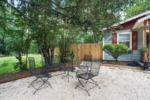 An outdoor seating area with metal chairs and a table, surrounded by trees and a wooden fence. - Storybook Cottage Near Downtown Hattiesburg-Family Friendly (Hattiesburg)