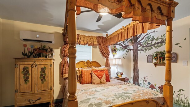 Una cama con dosel con un mural de un árbol en la pared, un armario de madera con adornos de piñas y una alfombra estampada.