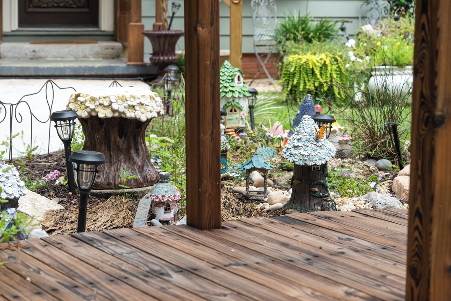 Un giardino con terrazza in legno, casette decorative a forma di fungo e piccole lanterne.