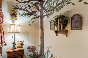 Ein Zimmer mit einer Wandmalerei eines Baumes, einer Kuckucksuhr, einer Lampe und einem Regal mit Pflanzen und einem gerahmten Bild.