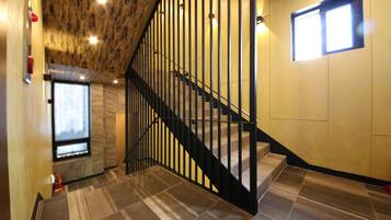 Una escalera con barandilla negra, una ventana a la izquierda y un muro con diseño texturizado.
