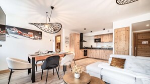 En moderne stue med en hvid sofa, et spiseområde med et træbord og et køkken med træskabe.