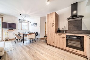 Une cuisine moderne avec des meubles en bois, un four encastré et un coin repas comprenant une table et des chaises.