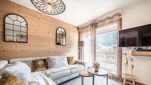 En moderne stue med en sofa, et rundt bord og et fjernsyn monteret på væggen.