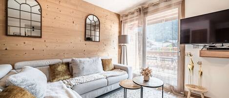 A modern living room with a sofa, a small round table, and a TV mounted on the wall.