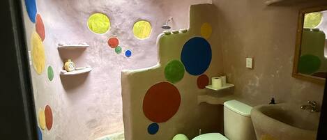 A bathroom with a toilet, sink, and mirror. There are colorful circles on the walls and ceiling.